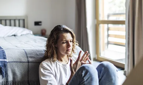 Burnout can be a product of stress from nurses’s work: a woman with a stressed expression on her face sits on the floor and absently examines her hands