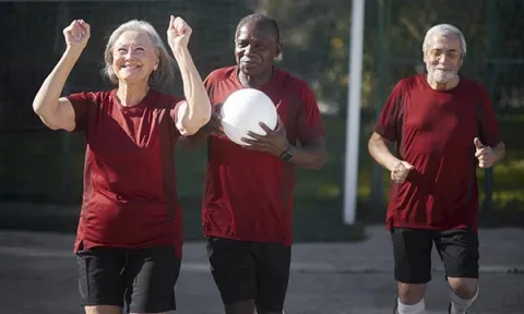 An older woman celebrates a walking football victory with her two male teammates (one of whom is holding a football): activities like this can be an important part of healthy ageing