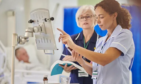 Nursing student or young nurse checks medication at patient’s bedside, while senior nurse checks her work, holding the BNF