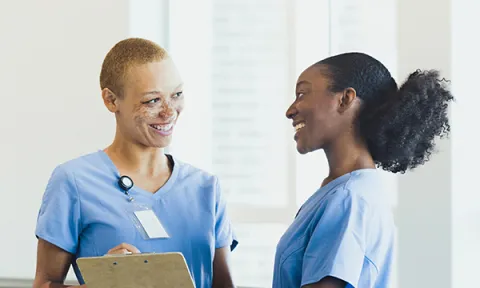 Two female nurses smile and chat to each other: Black History Month has the theme of reclaiming narratives and nursing staff should take the chance to share their nursing stories