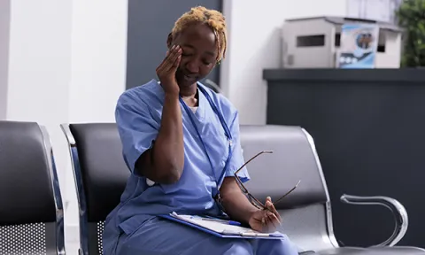A nurse sitting in a workplace setting rubs her eyes as if feeling tired after a shift