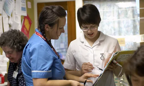 Outdated nursing practice: a nursing student on placement holds a patient’s chart as she asks a senior nurse some questions about it