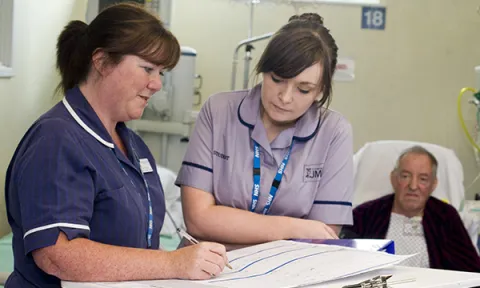 Band 6 nurse roles: senior ward nurse supports more junior nurse at patient’s bedside