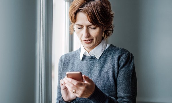 woman stands by window reading her phone