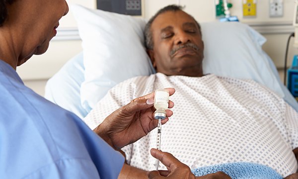 Nurse prepares to administer IV medicines to male patient lying in hospital bed