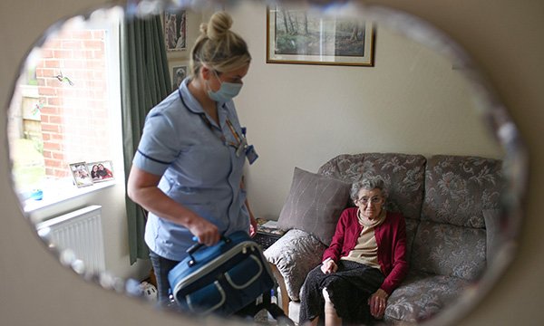 Image shows a community nurse in PPE tending to a patient in their home during the COVID-19 pandemic