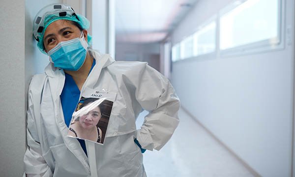 A nurse in PPE stands slumped against a corridor wall