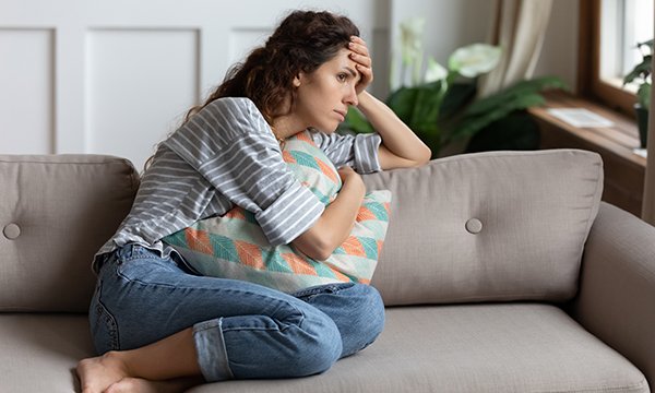 Picture shows a young woman sitting on a sofa looking pensive
