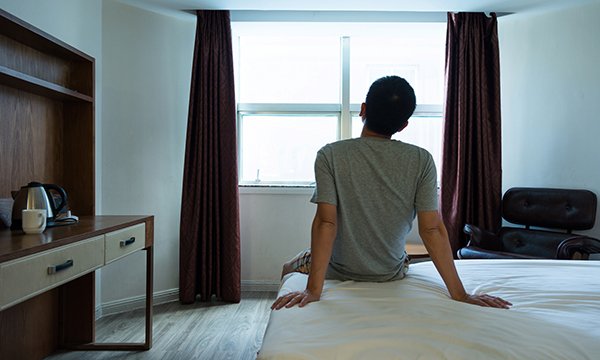 Picture shows someone seen from behind sitting on a bed and looking out of a window