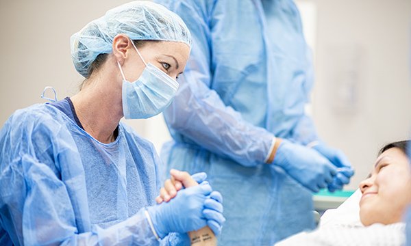 Picture shows a nurse sitting at a patient's bedside and holding their hand
