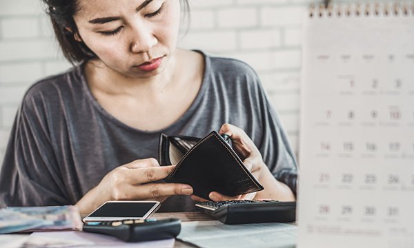Picture shows a young woman looking in her purse, which appears empty