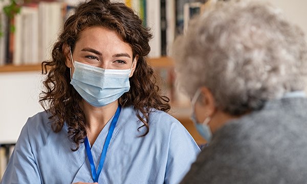 social care worker wearing face mask has a conversation with a client