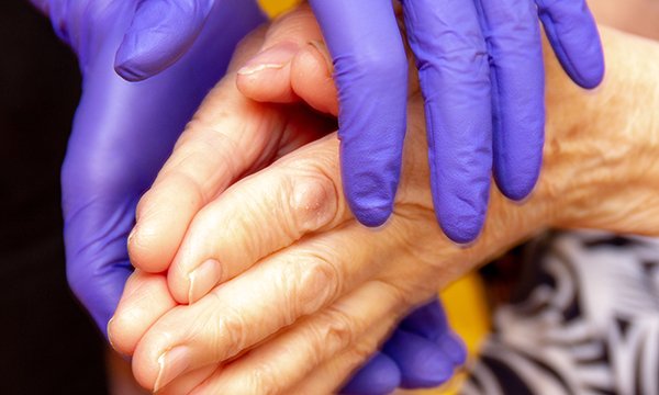 glove hands of a healthcare worker placed on hand of a patient