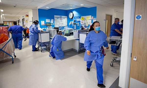 A busy hospital reception area with nurses checking documents or on their way to other areas 