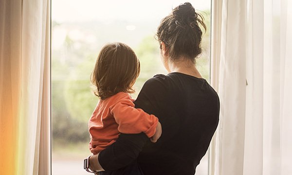 Woman holding a young child standing next to a window