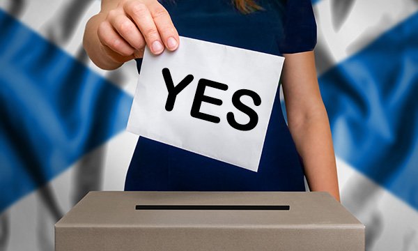 Unidentifiable woman standing in front of the flag of Scotland places 'Yes' vote in ballot box as RCN members in Scotland vote to accept NHS pay offer
