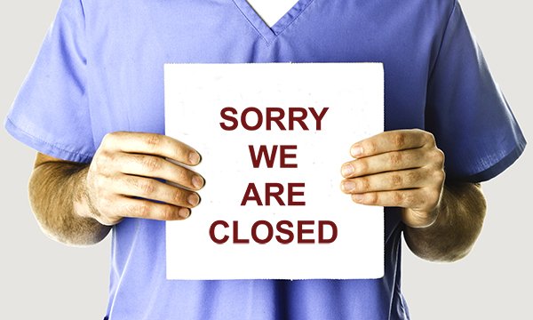 Nurse in scrubs seen from neck down, holds sign that reads 'Sorry we are closed' – community hospital in Wales has shut ward because it can't recruit nurses
