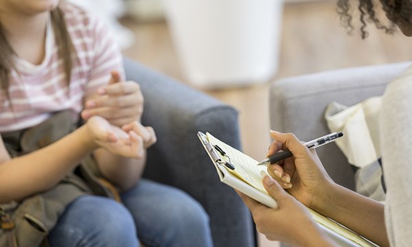 A healthcare professional with notebook writes notes while a woman speaks
