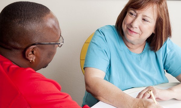 Nurse and service user sit at table talking, the nurse smiling as she takes notes