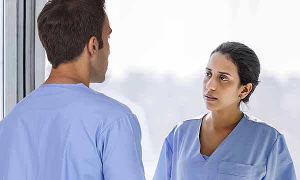 Two nurses in conversation, the one facing the camera looking perplexed
