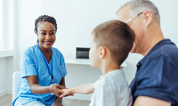 A nurse holds hands with a child who is sitting on their father’s lap