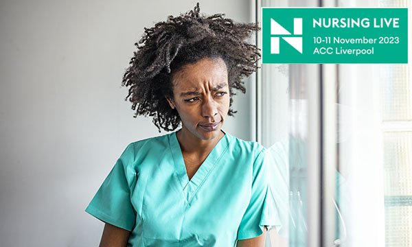 A nurse in green scrubs looks out a window looking pensive and anxious