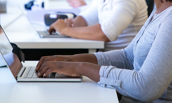 People, faces unseen, sit in a row working on computers