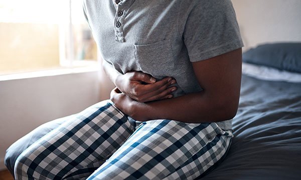 Someone sitting on the edge of a bed and holding their stomach in painv