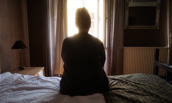 Photo of woman in dark room looking out of window, illustrating story about nurses from India living in poor conditions in the UK