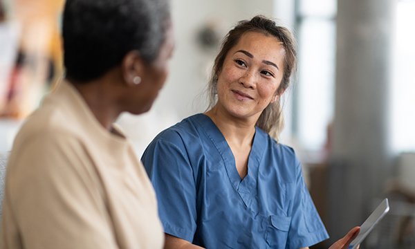 A nurse smiles at a patient as she shows her some information on a tablet