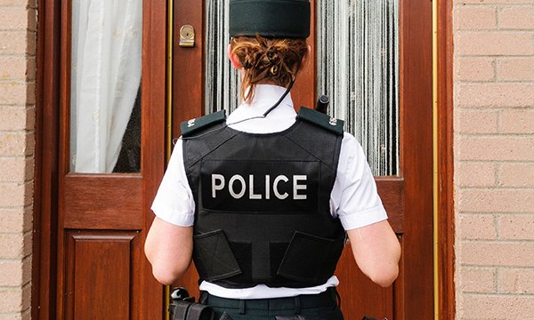 A uniformed police officer standing outside a front door