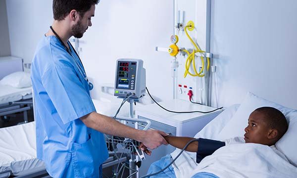 A nurse monitors a child’s pulse and blood pressure as they lie in a hospital bed