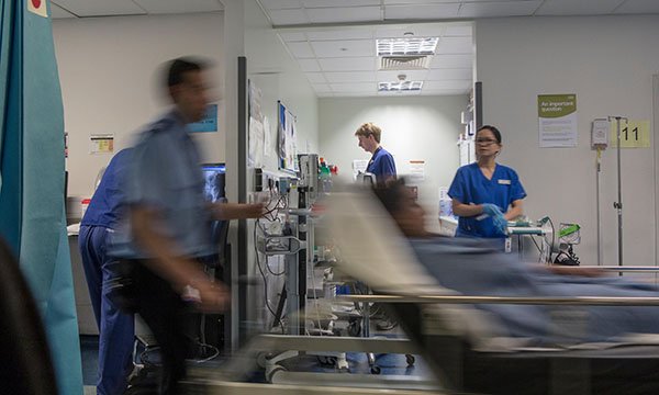 Scene at a busy hospital with medics engaged in various tasks as a trolley with a patient on it is pushed past