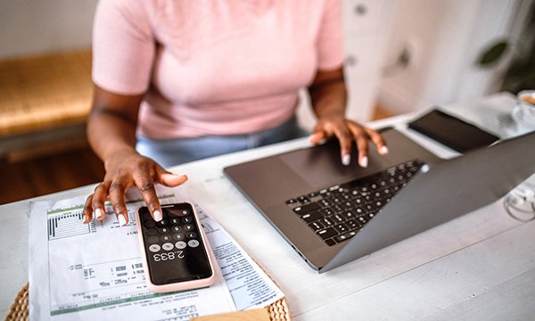 A woman uses the calaculator function on her phone while working at a computer