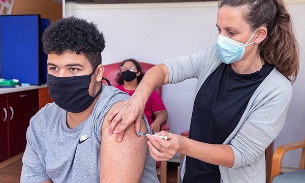 Senior clinical lead for children and young people with learning disabilities Rebecca Crossley stands next to a service user she is vaccinating, both wearing masks