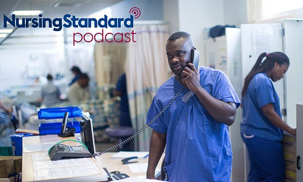 A nurses stands holding the phone at a hospital nurses' station while others are busy in the backgroundv