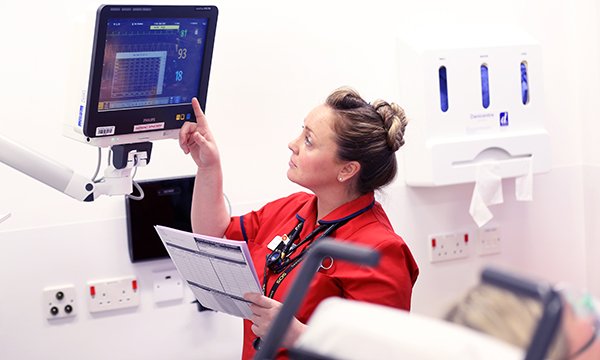 Nurse reads a vital signs monitor at patient’s bedside. This is key information when assessing level of risk for a person with sepsis