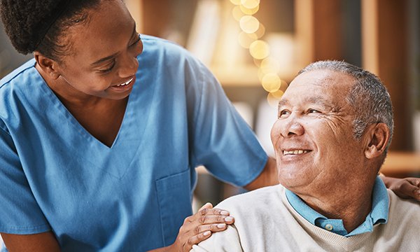  Nurse behind seated patient stoops slightly and has her hands on his shoulders to express warmth and reassurance. Touch is a powerful way to show compassion in nursing