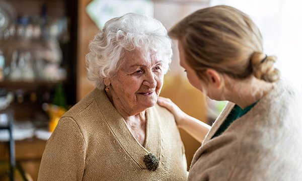 Older woman stands facing younger woman, possibly her daughter who has a supportive hand on her shoulder. Carer's leave is now a right, which will support the nurse workforce