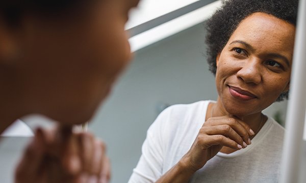A smiling woman appears deep in thought as she looks at her reflection in a mirror