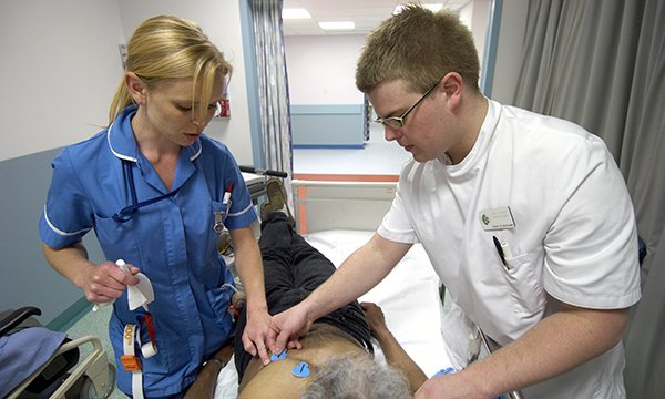 Nursing student is mentored by a nurse as he places ECG leads on the chest of a prone patient