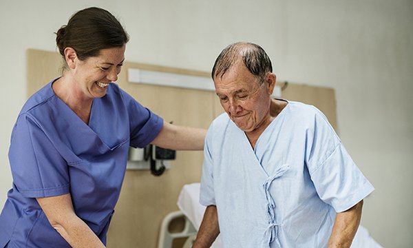 Smiling nurse helps patient get up from bed, showing how ward nurse intervention is important in preventing inpatient falls