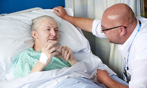 A learning disability liaison nurse talks to an older person in a hospital bed