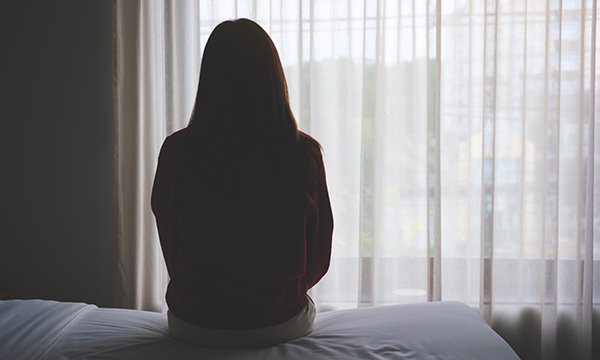 Person in shadow looking out of window, illustrating story about nurse and midwife suicides