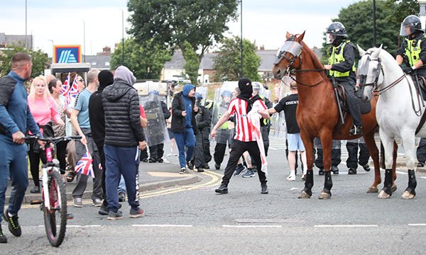 Filipino nurses targeted in Sunderland riots: a man in a mask stands stands next to a police horse as riot police confront protestors in the city centre on Friday