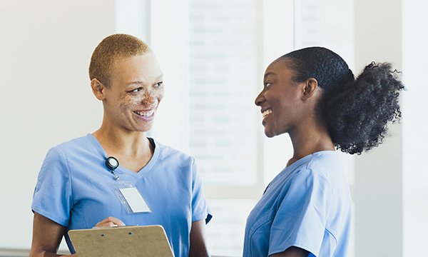 Two female nurses smile and chat to each other: Black History Month has the theme of reclaiming narratives and nursing staff should take the chance to share their nursing stories