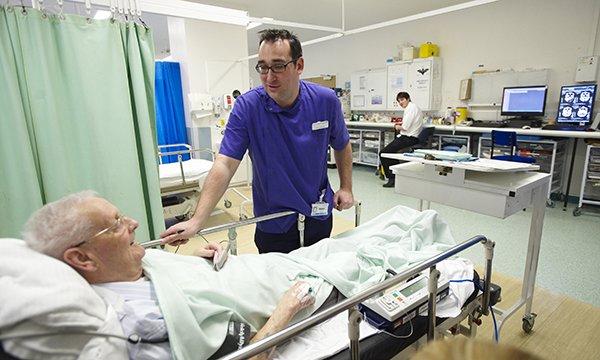 A 2022 study found that 75% of people living with dementia have at least one unplanned hospital admission following diagnosis.  An emergency department nurse keeps a close eye on an older patient lying in a hospital bed