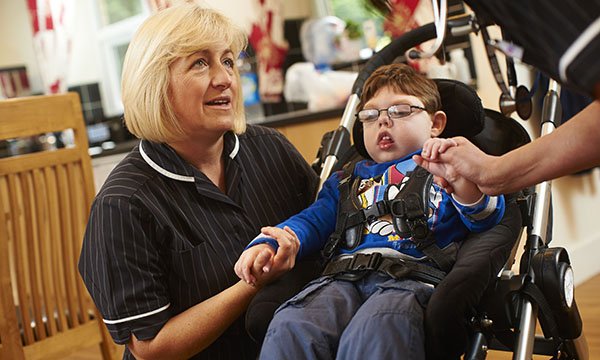A nurse holds the hand of an infant sitting in a pushchair as she talks to a family member. Learning disability nurses need to be champions for postural care.