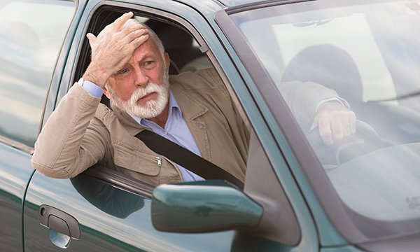 A driver leans out of the window of his car and puts a hand on his brow in confusion. Unsafe driving is an area of risk for accidental self-harm or harm to others.