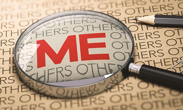 Narcissistic personality traits include self-worth being a top priority. Magnifying glass hovers over words in black on a page and focuses on the word ME, which is highlighted in red